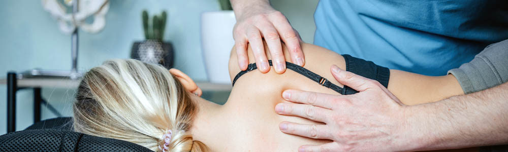 Young woman laying on her side, facing away from the camera; close-up of practitioner's hands working on her shoulder and upper back